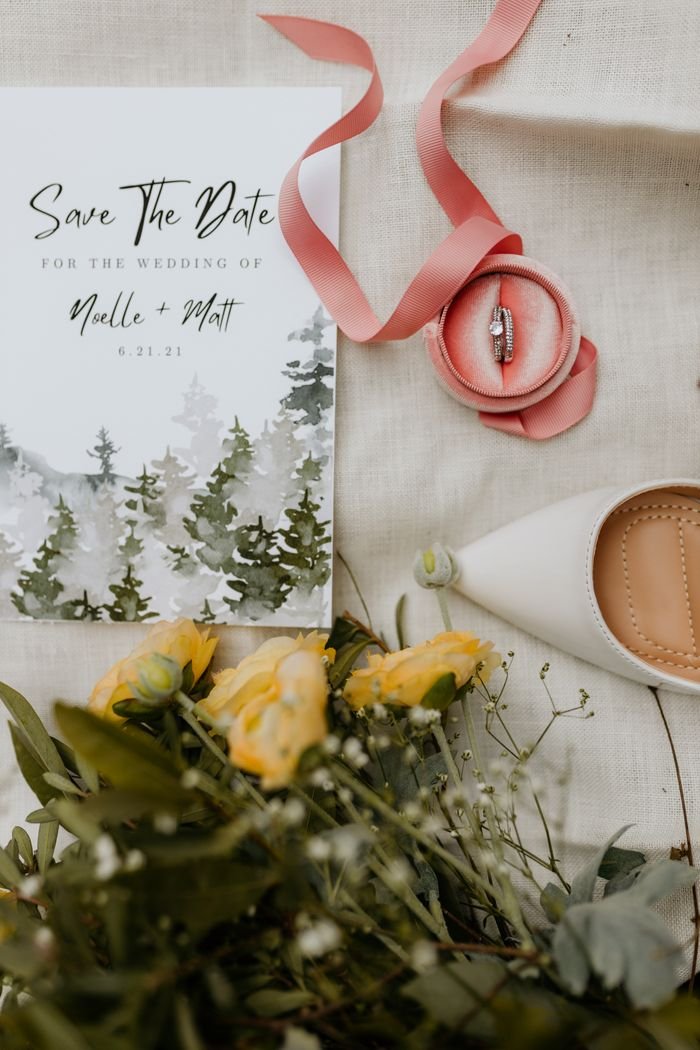 our-story Stylish wedding setup with invitation, rings, flowers, and shoes.