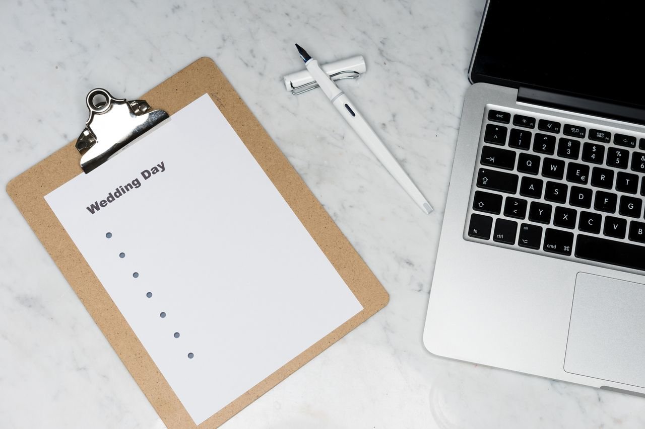 who-we-are Flat lay of a wedding planning setting with clipboard, laptop, and pen.